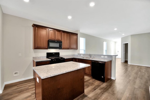 kitchen with black appliances, sink, a kitchen island, dark wood-type flooring, and light stone counters