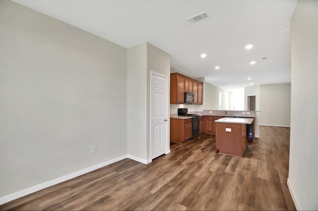 kitchen with kitchen peninsula, a kitchen bar, dark hardwood / wood-style floors, black appliances, and a center island