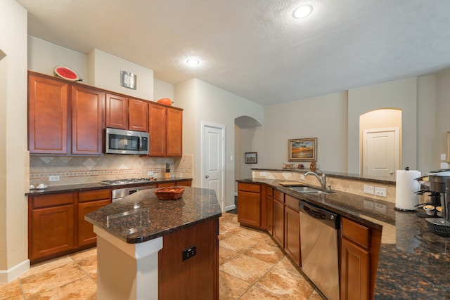 kitchen with sink, a kitchen island, appliances with stainless steel finishes, and dark stone countertops