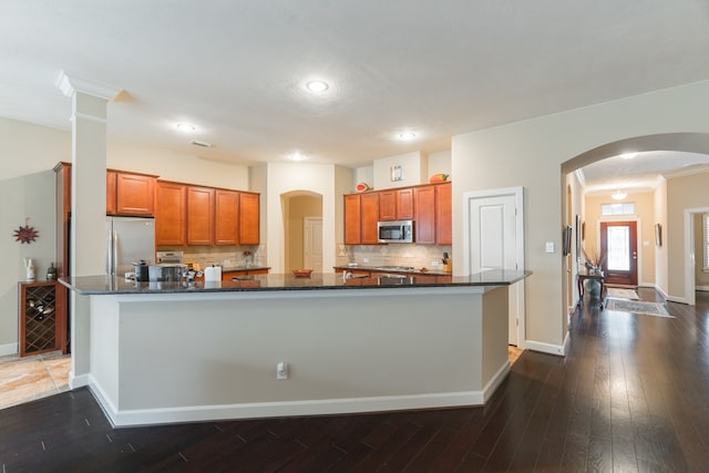 kitchen featuring decorative backsplash, dark hardwood / wood-style floors, dark stone counters, crown molding, and appliances with stainless steel finishes