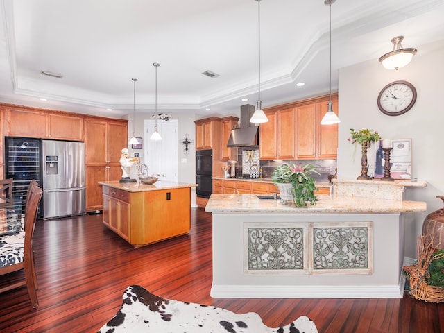 kitchen with a tray ceiling, decorative light fixtures, dark wood-type flooring, stainless steel fridge with ice dispenser, and ventilation hood