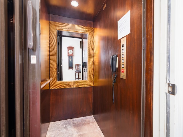 hallway featuring wood walls, tile patterned floors, and elevator