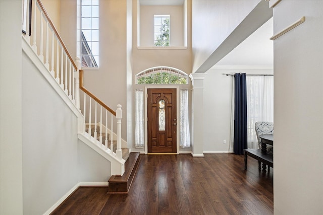 foyer entrance with stairs, baseboards, wood finished floors, and a towering ceiling
