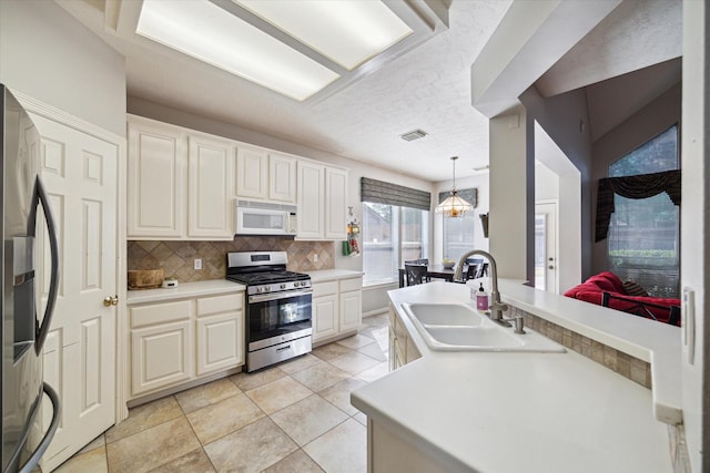 kitchen with backsplash, appliances with stainless steel finishes, hanging light fixtures, sink, and light tile patterned flooring