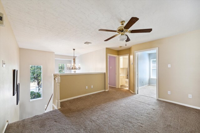 carpeted spare room featuring ceiling fan with notable chandelier and a textured ceiling