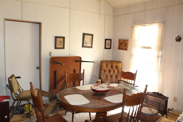 dining room featuring vaulted ceiling and wooden walls