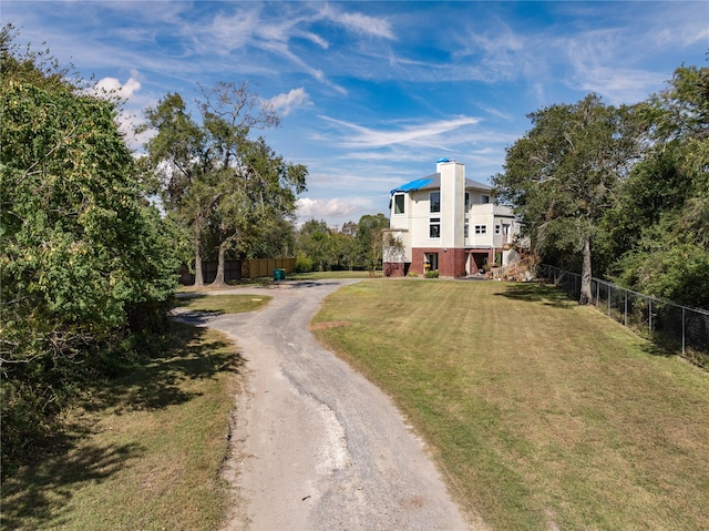 view of front of house with a chimney, dirt driveway, fence, and a front lawn