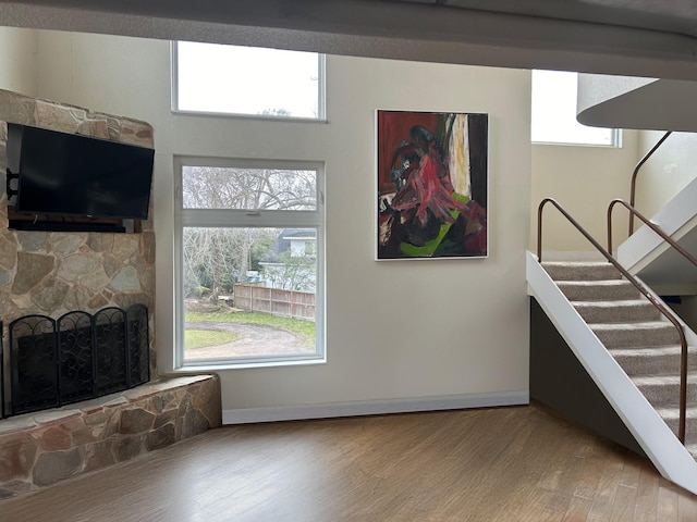 living room with a wealth of natural light, a stone fireplace, stairway, and wood finished floors