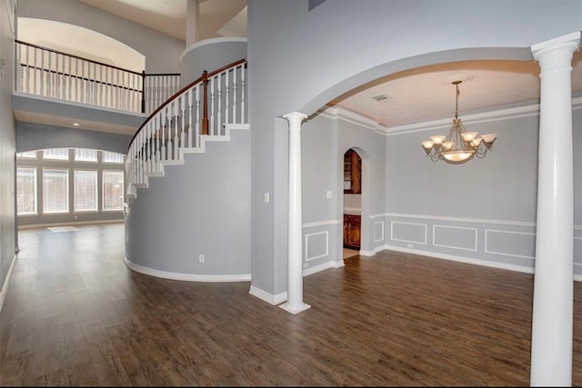 interior space with decorative columns, dark hardwood / wood-style flooring, a high ceiling, crown molding, and a notable chandelier