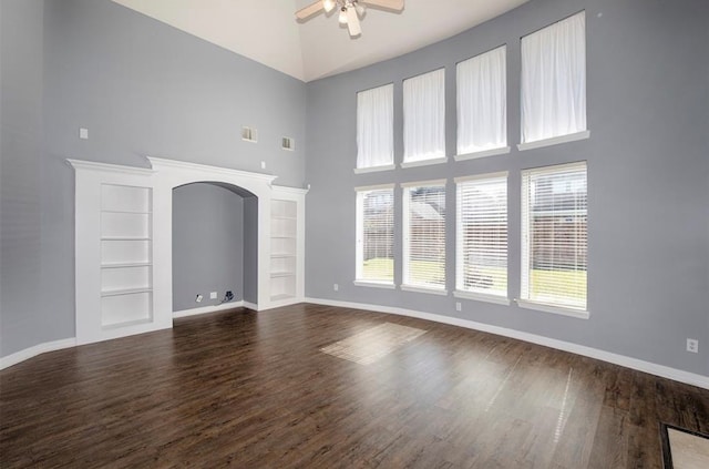 unfurnished living room with ceiling fan, hardwood / wood-style flooring, a towering ceiling, and built in shelves