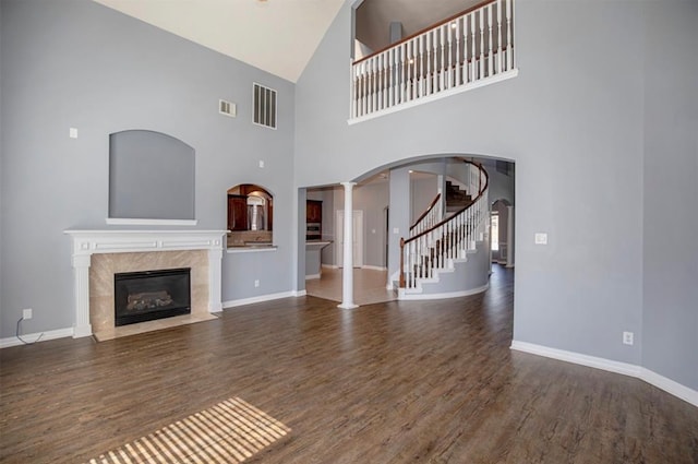 unfurnished living room featuring decorative columns, a towering ceiling, dark hardwood / wood-style flooring, and a fireplace