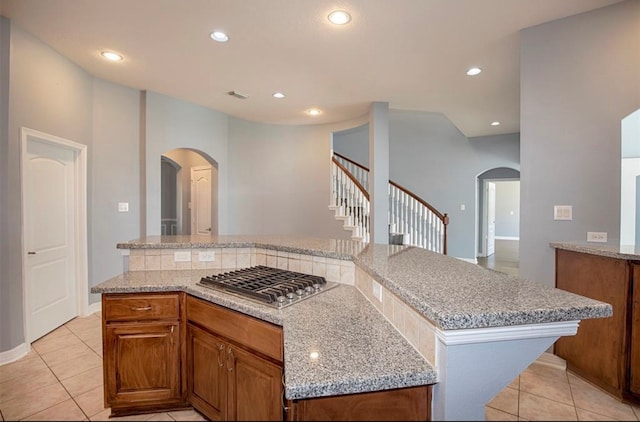 kitchen featuring stainless steel gas stovetop, light stone countertops, a kitchen island, and light tile patterned floors