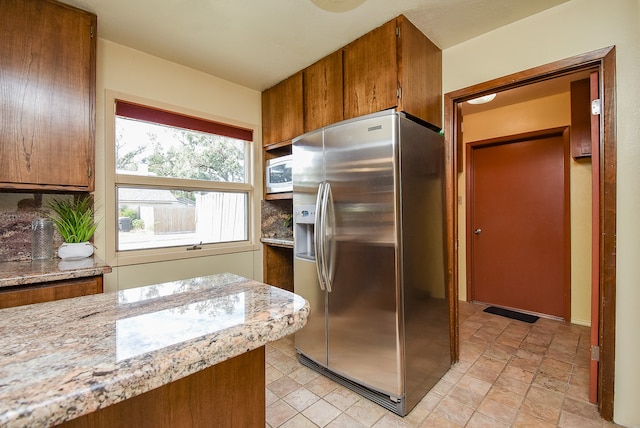 kitchen with decorative backsplash, light stone countertops, stainless steel refrigerator with ice dispenser, and built in microwave