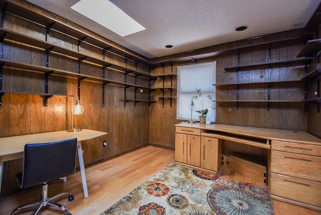 office featuring built in desk, a textured ceiling, wooden walls, and light hardwood / wood-style flooring