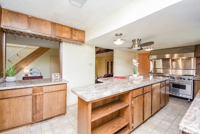 kitchen with wall chimney exhaust hood, ceiling fan, stainless steel range, a kitchen island, and light stone counters