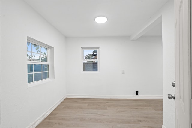 spare room with beam ceiling and light wood-type flooring