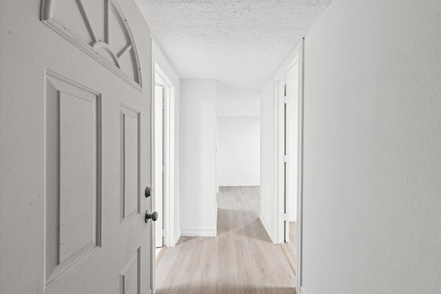 corridor with light hardwood / wood-style floors and a textured ceiling