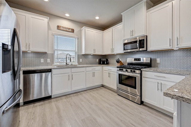 kitchen with light hardwood / wood-style flooring, white cabinets, appliances with stainless steel finishes, light stone counters, and tasteful backsplash