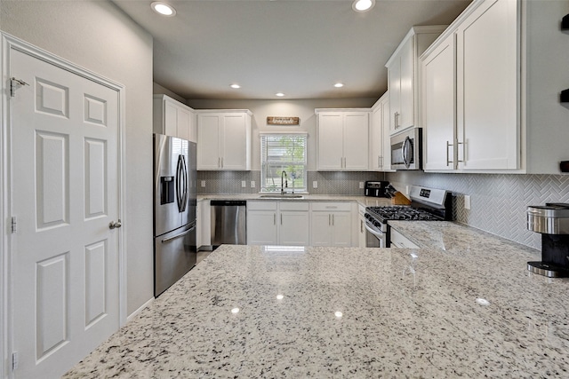 kitchen featuring tasteful backsplash, light stone counters, appliances with stainless steel finishes, white cabinetry, and sink