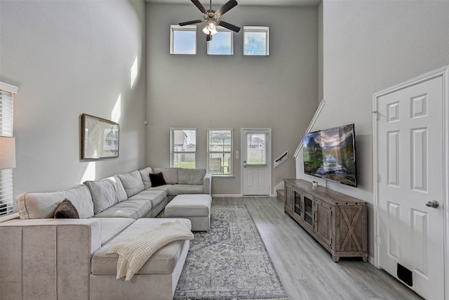 living room with a towering ceiling, light hardwood / wood-style flooring, a healthy amount of sunlight, and ceiling fan