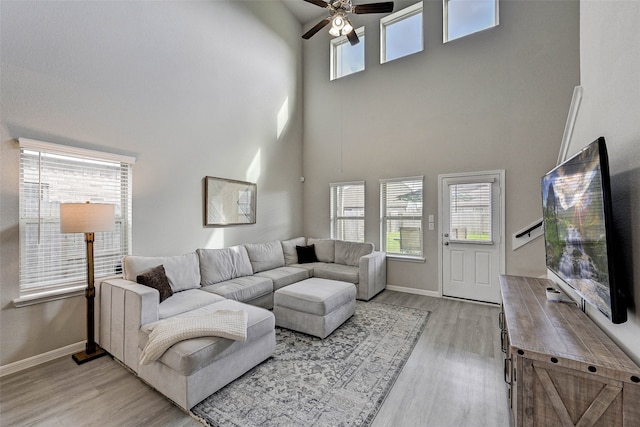 living room with a high ceiling, light wood-type flooring, and ceiling fan