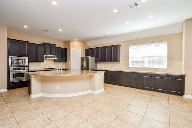 kitchen featuring backsplash, appliances with stainless steel finishes, a kitchen island with sink, and light tile patterned floors