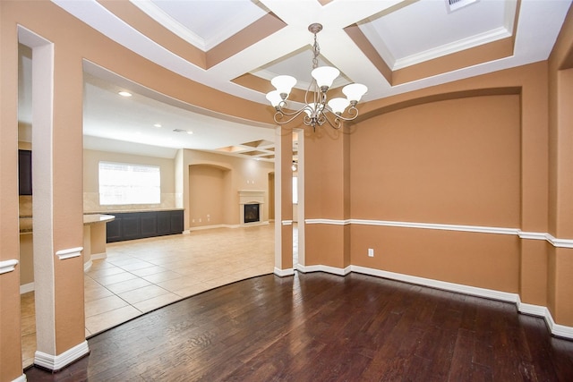 empty room featuring ornamental molding, coffered ceiling, hardwood / wood-style floors, and a notable chandelier