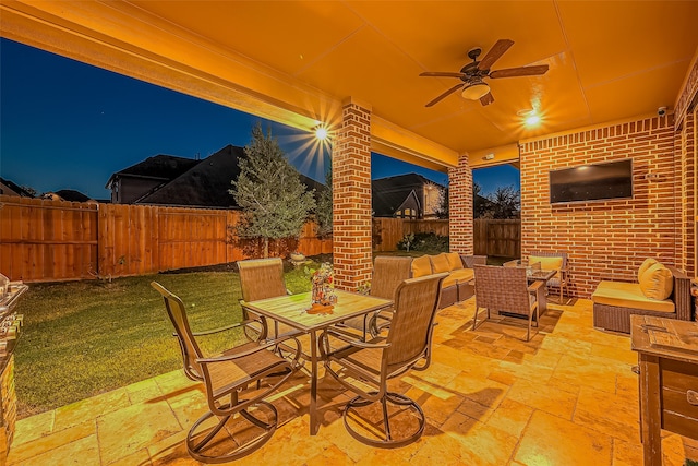 patio at night featuring an outdoor living space, a lawn, and ceiling fan