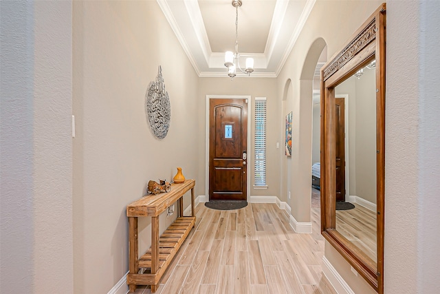 foyer entrance featuring light hardwood / wood-style flooring, ornamental molding, a notable chandelier, and a tray ceiling