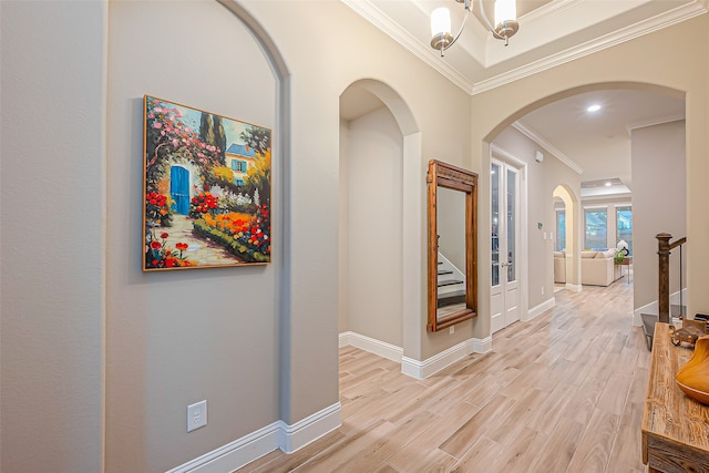 hall with light hardwood / wood-style floors, crown molding, and a chandelier