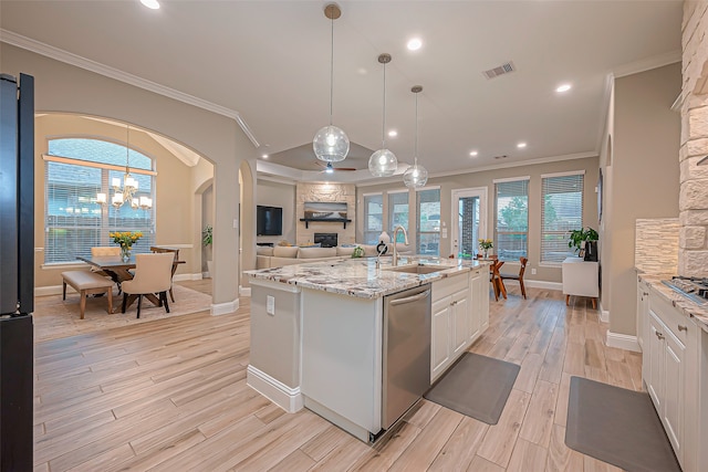 kitchen with light stone countertops, appliances with stainless steel finishes, sink, white cabinets, and a center island with sink