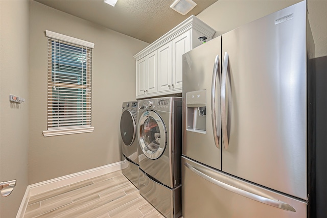 laundry room with independent washer and dryer, a textured ceiling, cabinets, and light hardwood / wood-style flooring