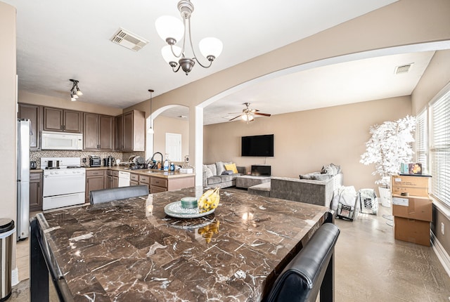 kitchen with kitchen peninsula, backsplash, ceiling fan with notable chandelier, decorative light fixtures, and white appliances