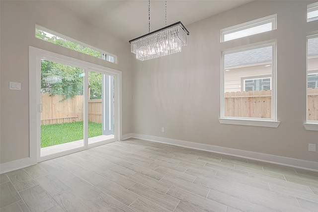 unfurnished dining area featuring an inviting chandelier, light wood-type flooring, and a wealth of natural light