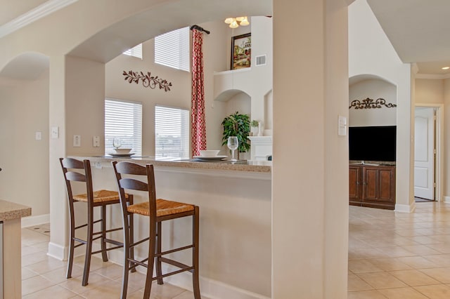 kitchen with a kitchen breakfast bar, light tile patterned flooring, a high ceiling, and ornamental molding