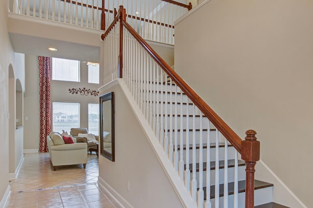 staircase with tile patterned flooring, a healthy amount of sunlight, and a high ceiling