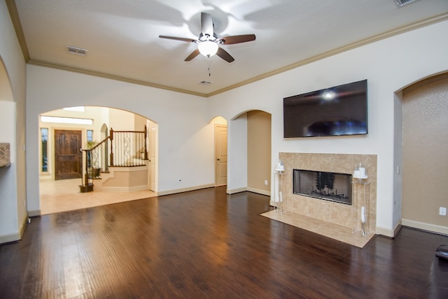 living room featuring crown molding, dark wood-type flooring, a tile fireplace, and ceiling fan