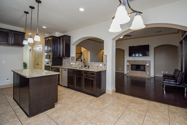 kitchen with appliances with stainless steel finishes, sink, a center island, dark brown cabinetry, and decorative light fixtures