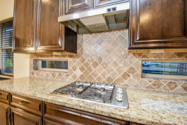 kitchen featuring stainless steel gas stovetop, light stone counters, and backsplash