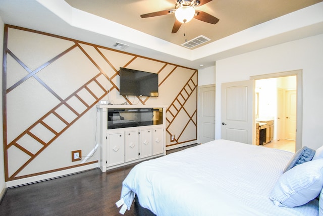 bedroom with dark hardwood / wood-style flooring, connected bathroom, a raised ceiling, and ceiling fan