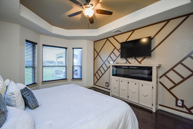 bedroom with dark hardwood / wood-style floors, a tray ceiling, and ceiling fan