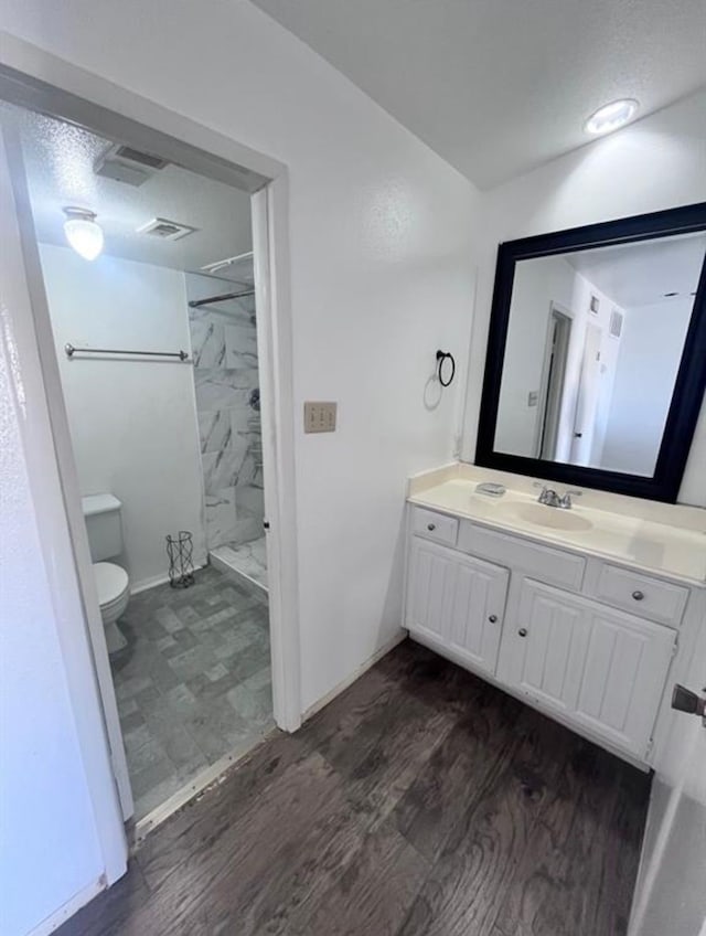 bathroom featuring toilet, vanity, a tile shower, and wood-type flooring