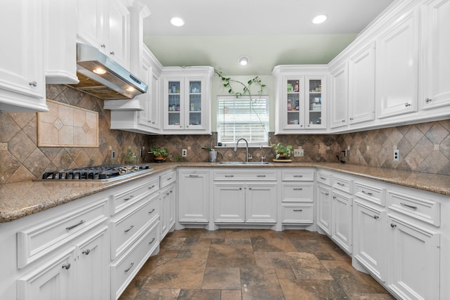 631 Apache St, Houston, TX 77022 - kitchen featuring a sink, under cabinet range hood, white cabinets, stainless steel gas cooktop, and dark stone finish floors