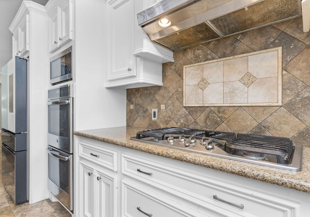 631 Apache St, Houston, TX 77022 - kitchen featuring premium range hood, stainless steel appliances, white cabinets, decorative backsplash, and light stone counters