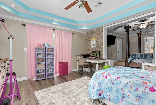 bedroom with a raised ceiling, ceiling fan, wood-type flooring, a fireplace, and crown molding