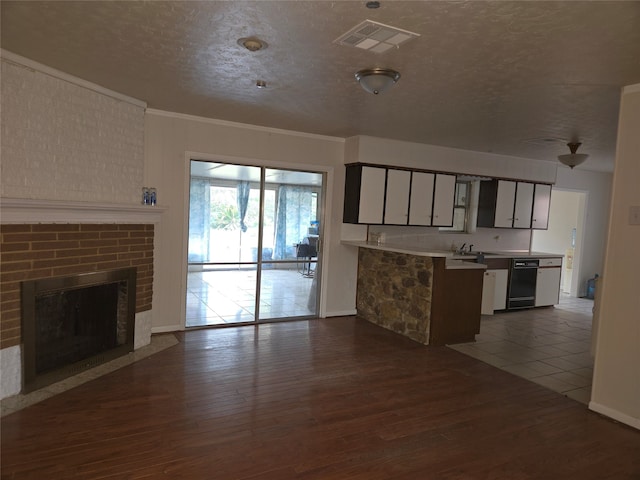 kitchen with black dishwasher, a textured ceiling, dark wood-type flooring, a fireplace, and crown molding