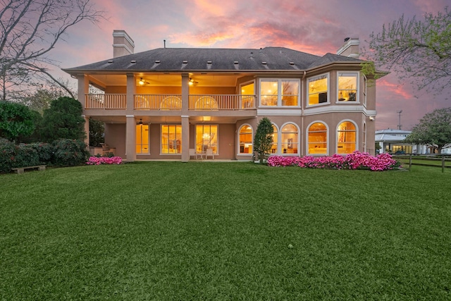 back house at dusk with a patio area, a yard, and a balcony