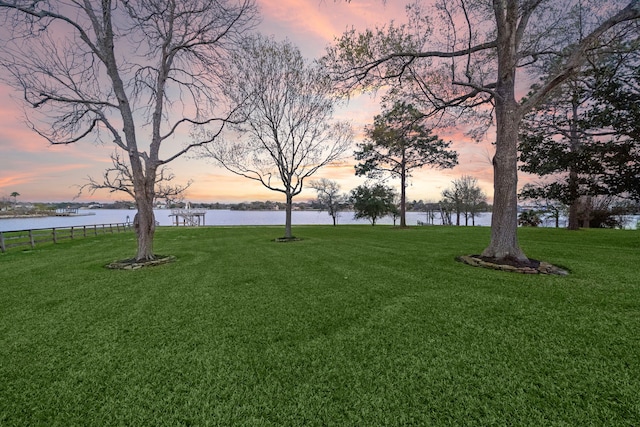 yard at dusk featuring a water view and fence