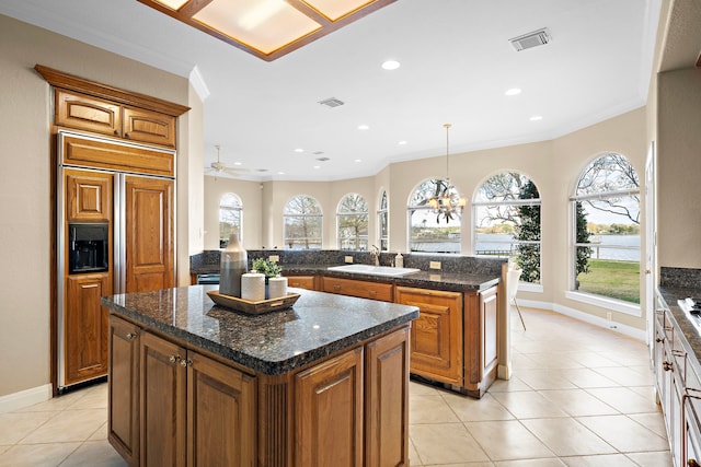 kitchen featuring a kitchen island, visible vents, crown molding, a sink, and paneled built in refrigerator