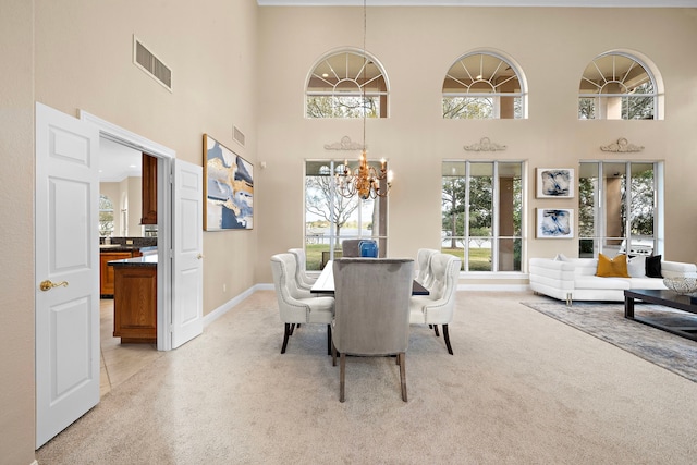 dining area with an inviting chandelier, visible vents, light carpet, baseboards, and a high ceiling